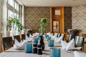 A dining table set with blue glassware, white napkins, and a black vase with a green plant.