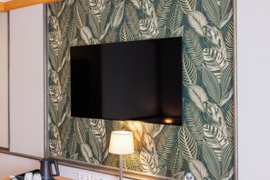 A flat-screen TV mounted on a wall with a leaf-pattern wallpaper.