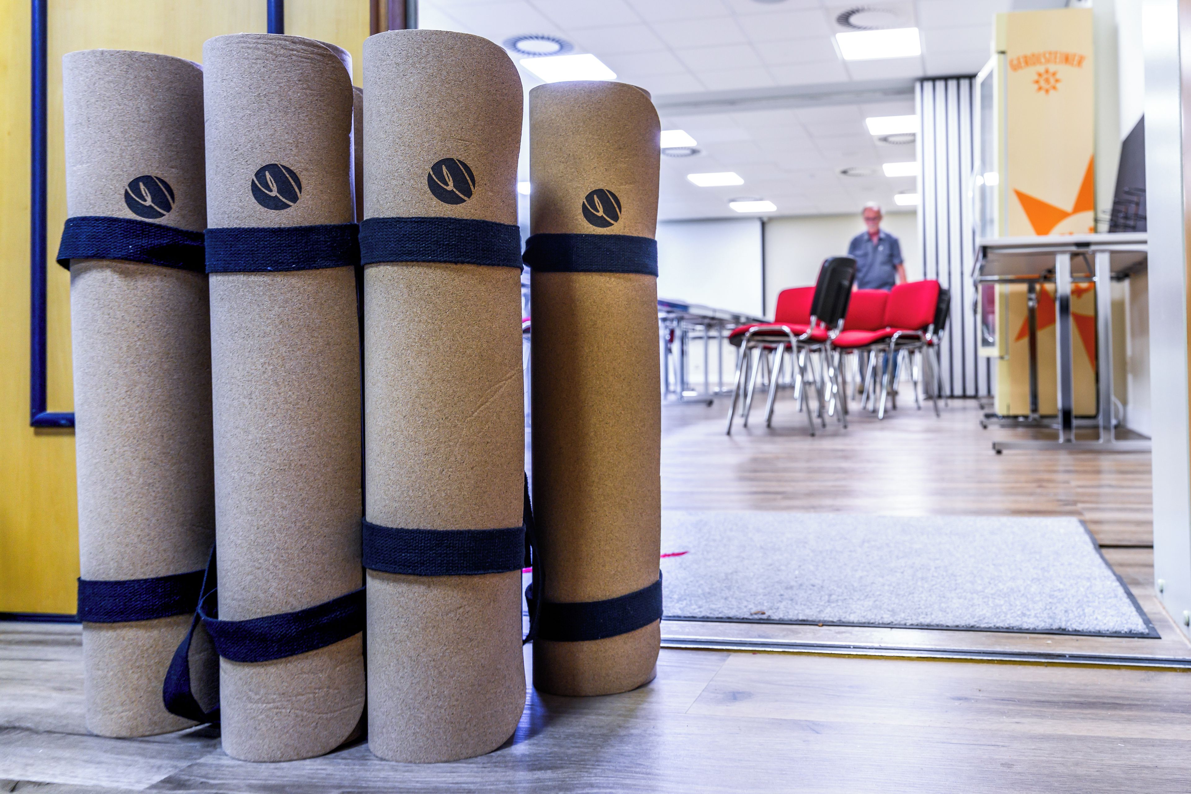 A row of cylindrical objects with a dark band, possibly luggage or storage items, in a room with chairs and a person in the background.