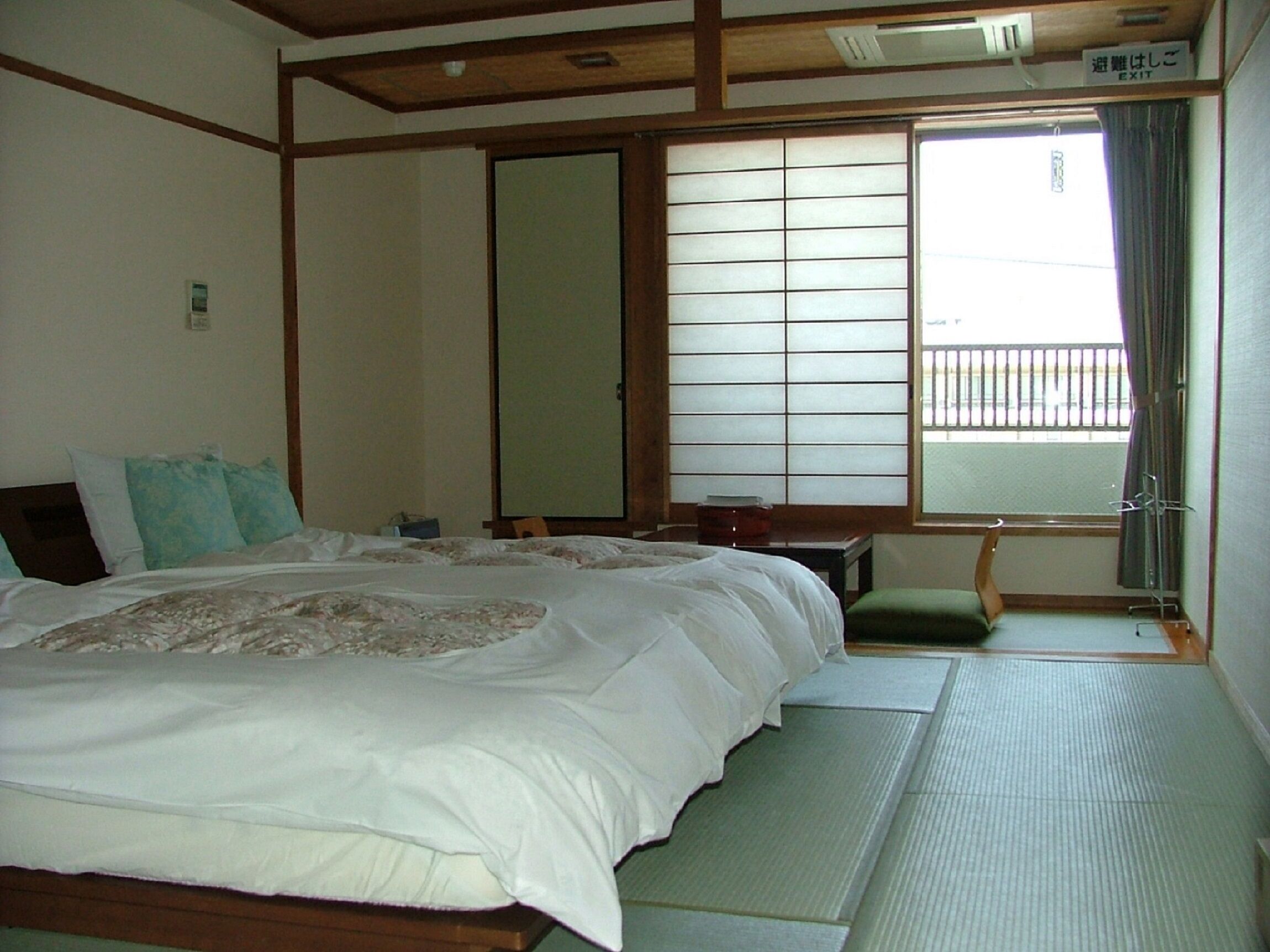 Une pièce de style japonais traditionnel, avec un sol recouvert de tatamis, un grand lit avec une literie blanche, une porte coulissante de type shoji et une vue sur un balcon.