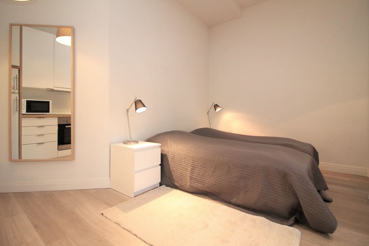 A bedroom with a bed, bedside lamps, a nightstand, a mirror, and a microwave.