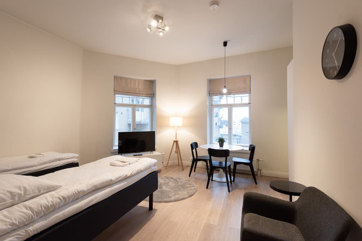 A hotel room with two beds, a desk, a chair, a TV, and a clock on the wall.