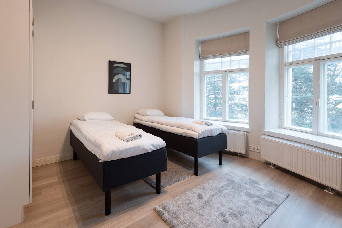 A bedroom with two single beds, a radiator, and a window with a view of trees.