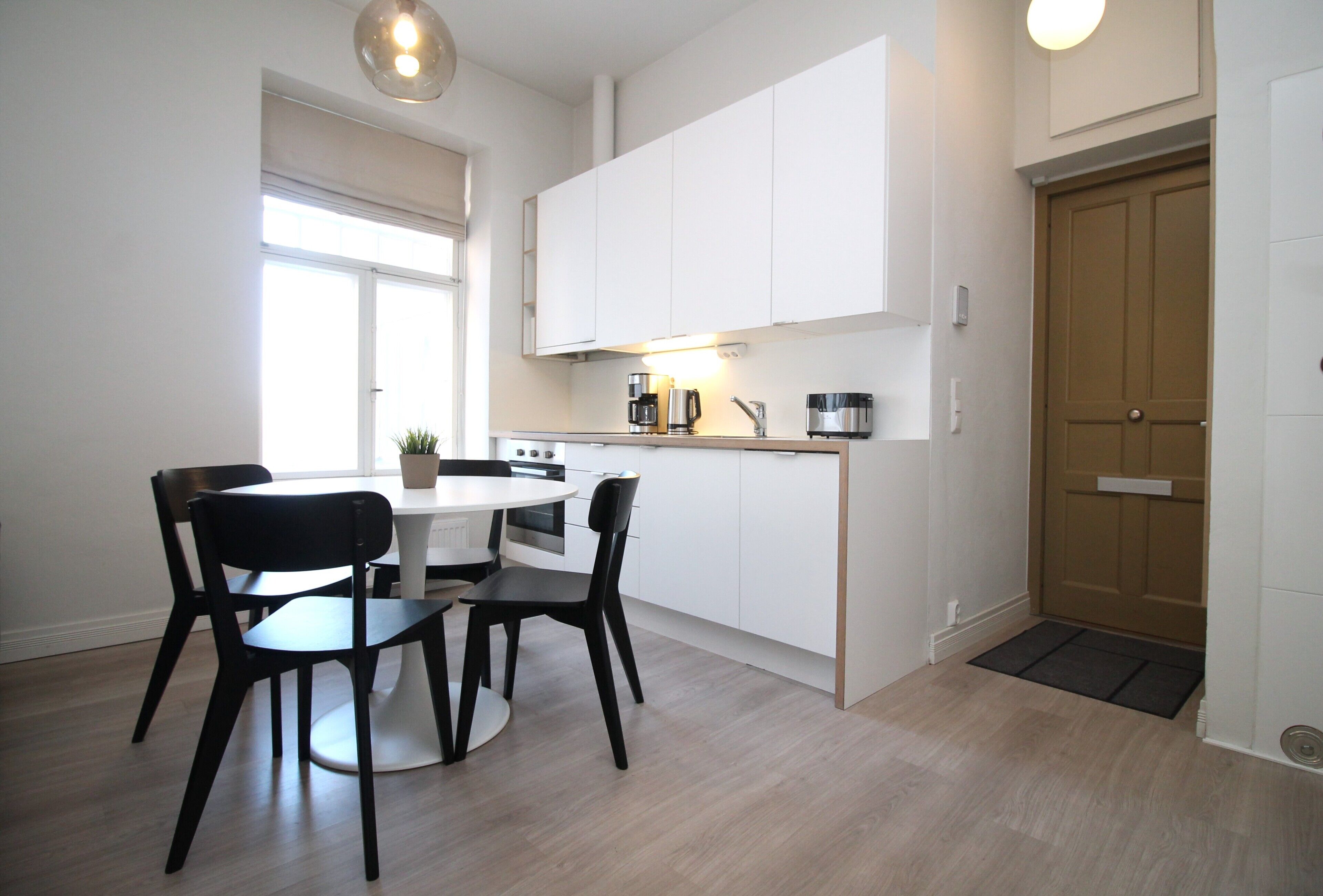 A modern kitchen with white cabinets, a dining table with chairs, and a wooden door.
