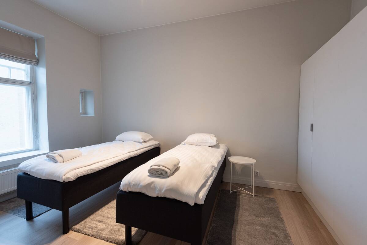 A bedroom with two single beds, a small white table, and a window with a view.