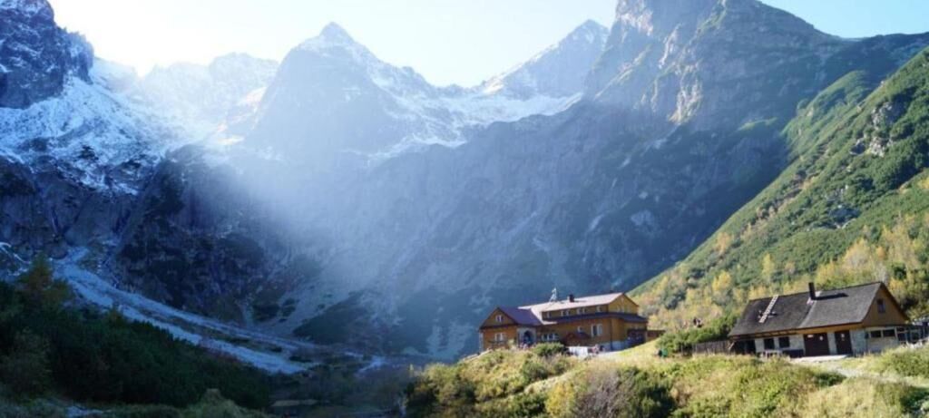 Una cabaña de montaña con vistas a picos nevados y un valle.