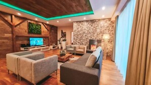 A modern living room with a fireplace, wooden beams, and a stone wall. - Hotel Crocus (Štrba)