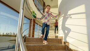 A child climbing stairs inside a building with a glass railing and a view of the outdoors. - Hotel Crocus (Štrba)
