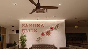 A reception area with a sofa and chairs, a ceiling fan, and a wall with 'SAKURA ELITE' signage. - Sakura Elite Hotel (Kuala Lumpur)