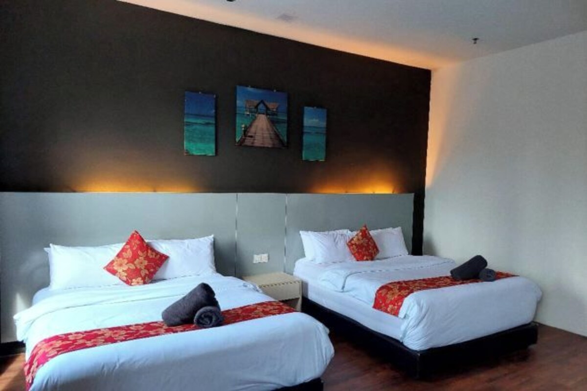 Une chambre d’hôtel avec deux lits, chacun agrémenté de draps blancs et d’oreillers décoratifs rouges. Trois tableaux encadrés sont accrochés au mur, au-dessus des lits.