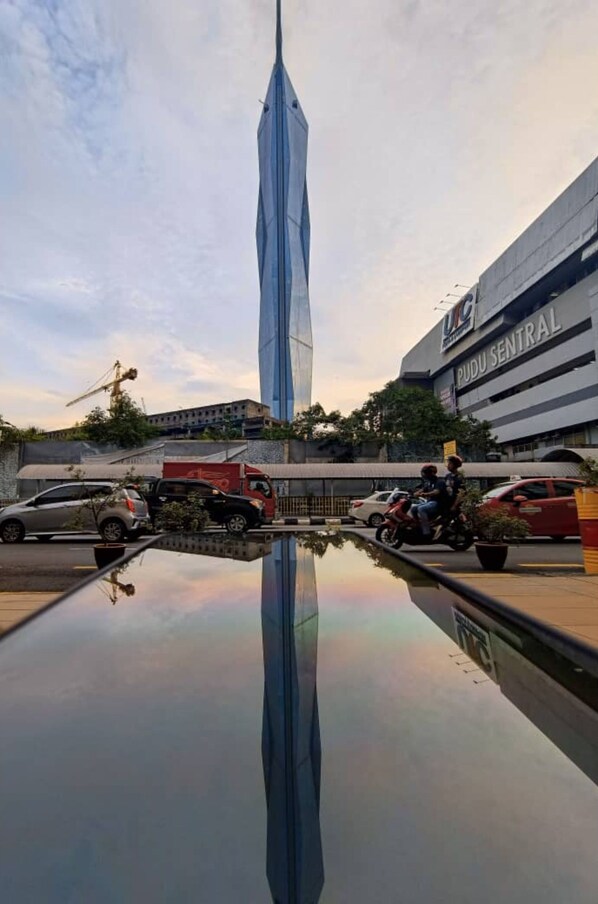A modern building with a unique, curved design, a parking lot with several cars and motorcycles, and a reflection pool.