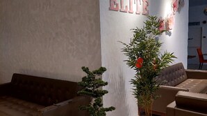A modern interior with a sofa, two potted plants, and a wall with 'SAKURA ELITE' signage. - Sakura Elite Hotel (Kuala Lumpur)