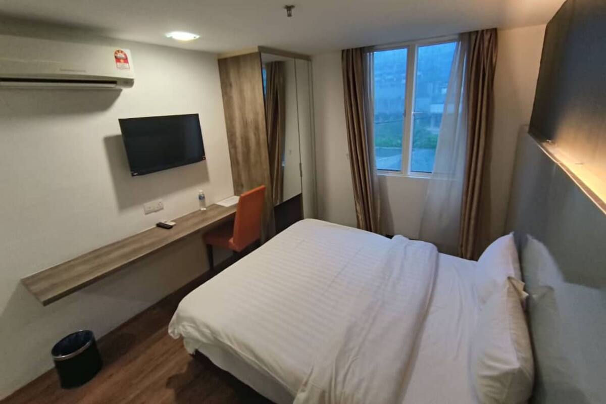 A hotel room with a bed, a desk with a chair, a television, and a window with curtains.