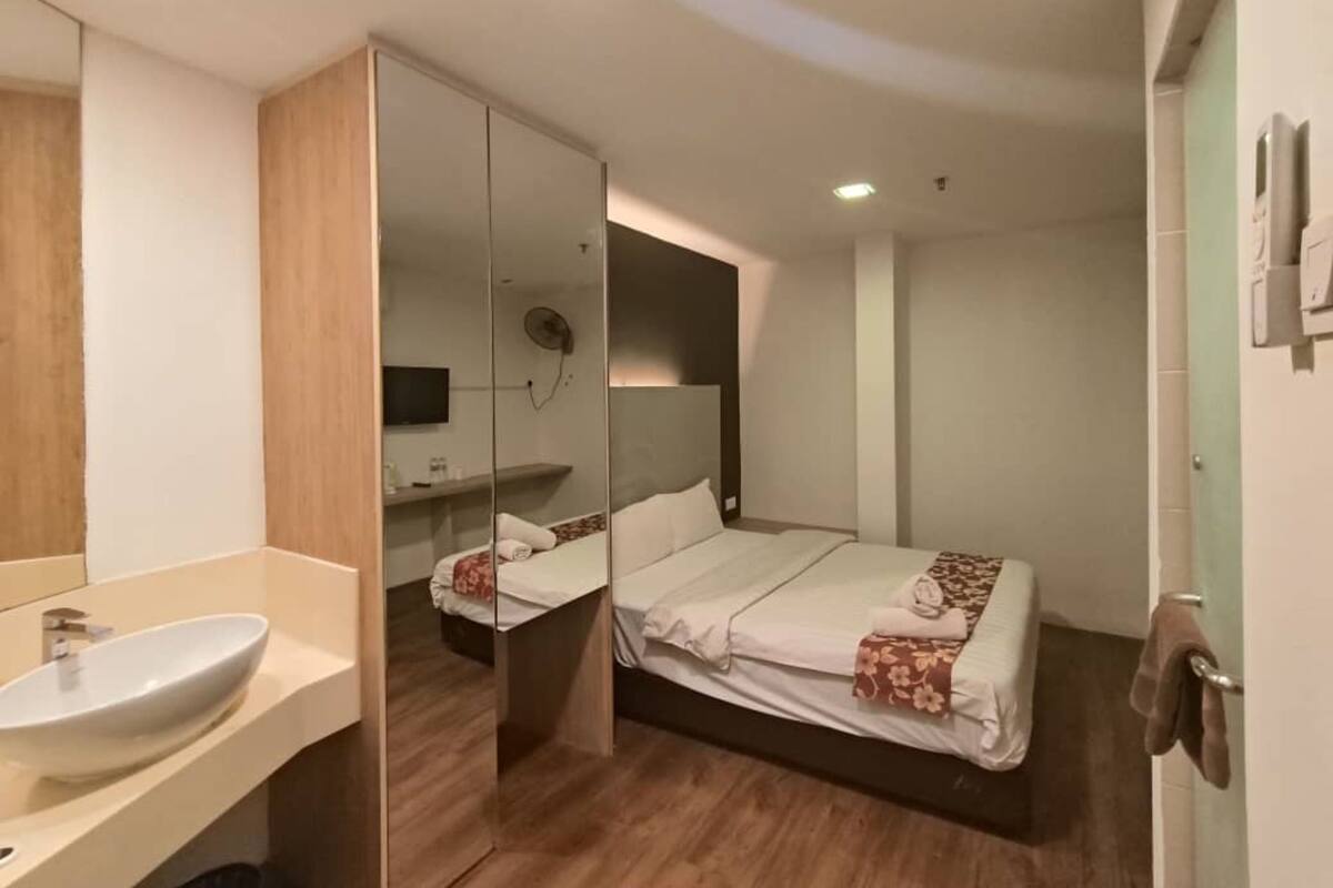 A modern hotel room with a large mirror, a bed with a floral bedspread, a bedside table, and a built-in TV.