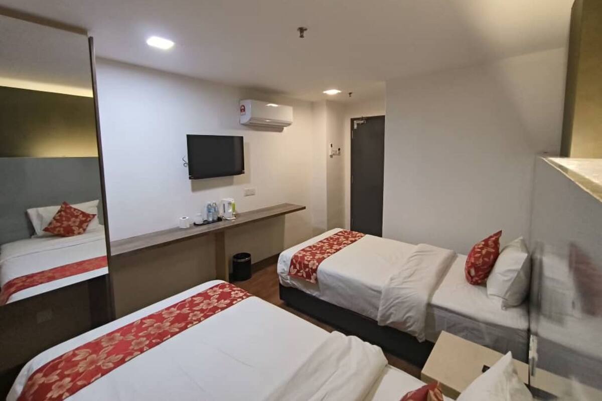 A hotel room with two beds, a TV, a desk, and a mirror.