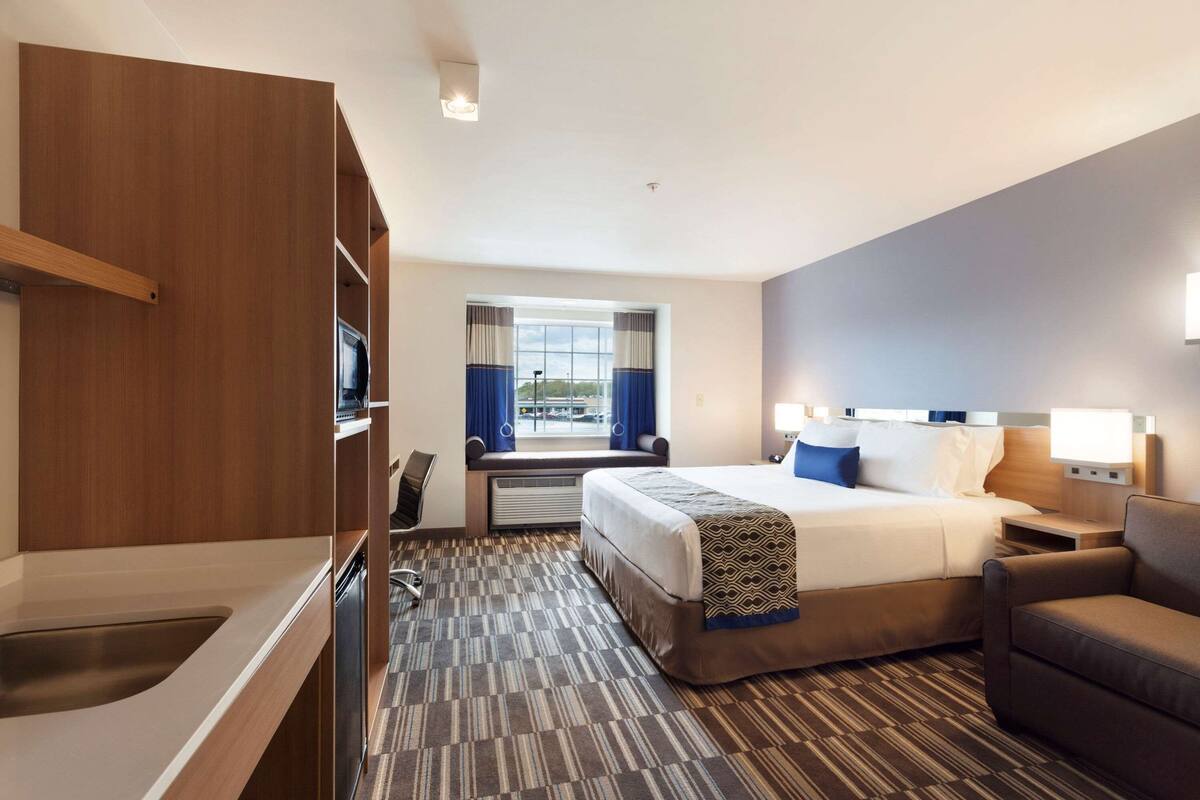 A hotel room with a bed, a sofa, a desk, and a window with curtains.