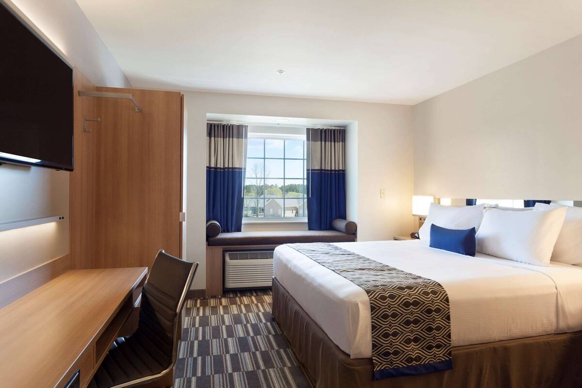 A hotel room with a bed, a desk, a chair, a TV, and a window with curtains.