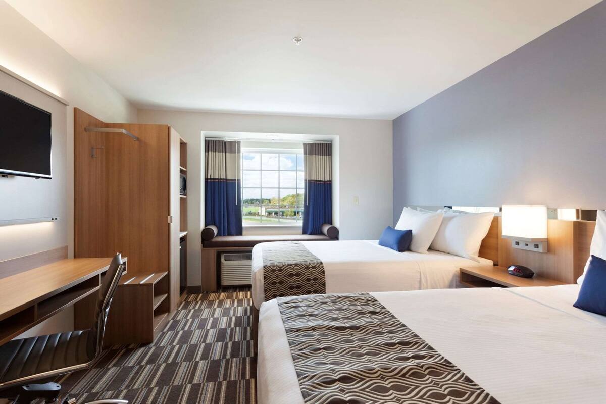 A hotel room with a bed, desk, TV, and a window with curtains.