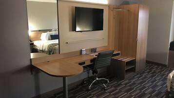 A hotel room with a desk, chair, and a large mirror reflecting a bed.
