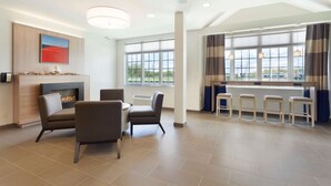 A modern hotel lobby with a fireplace, comfortable seating, a bar area, and large windows offering a view. - Microtel Inn & Suites By Wyndham Georgetown Delaware Beaches (Georgetown)