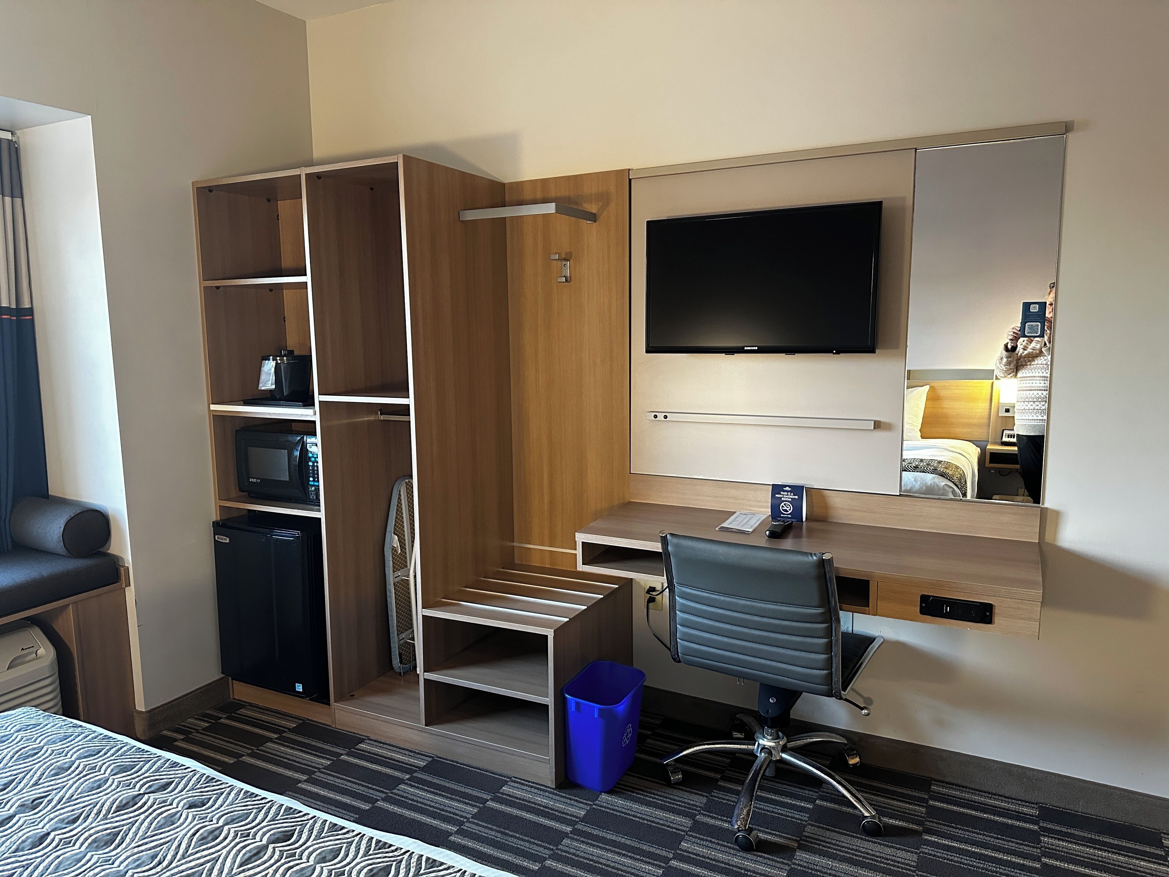 Habitación de hotel con un armario de madera, un escritorio con una silla, un televisor y una cama con colcha estampada.