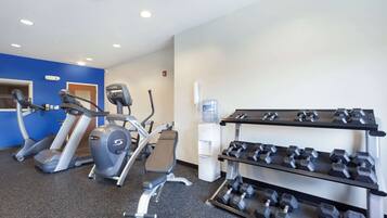 Un gimnasio con cintas de correr, elíptica y un estante con mancuernas.