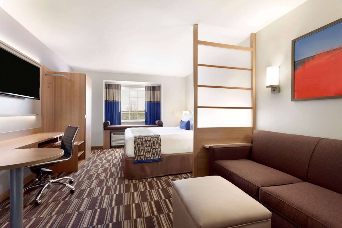 A hotel room with a desk, chair, bed, couch, and a TV.