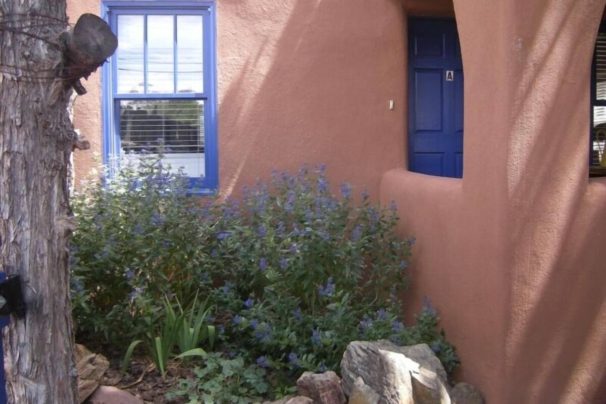 A building with a blue door and window, surrounded by a garden with purple flowers and rocks.
