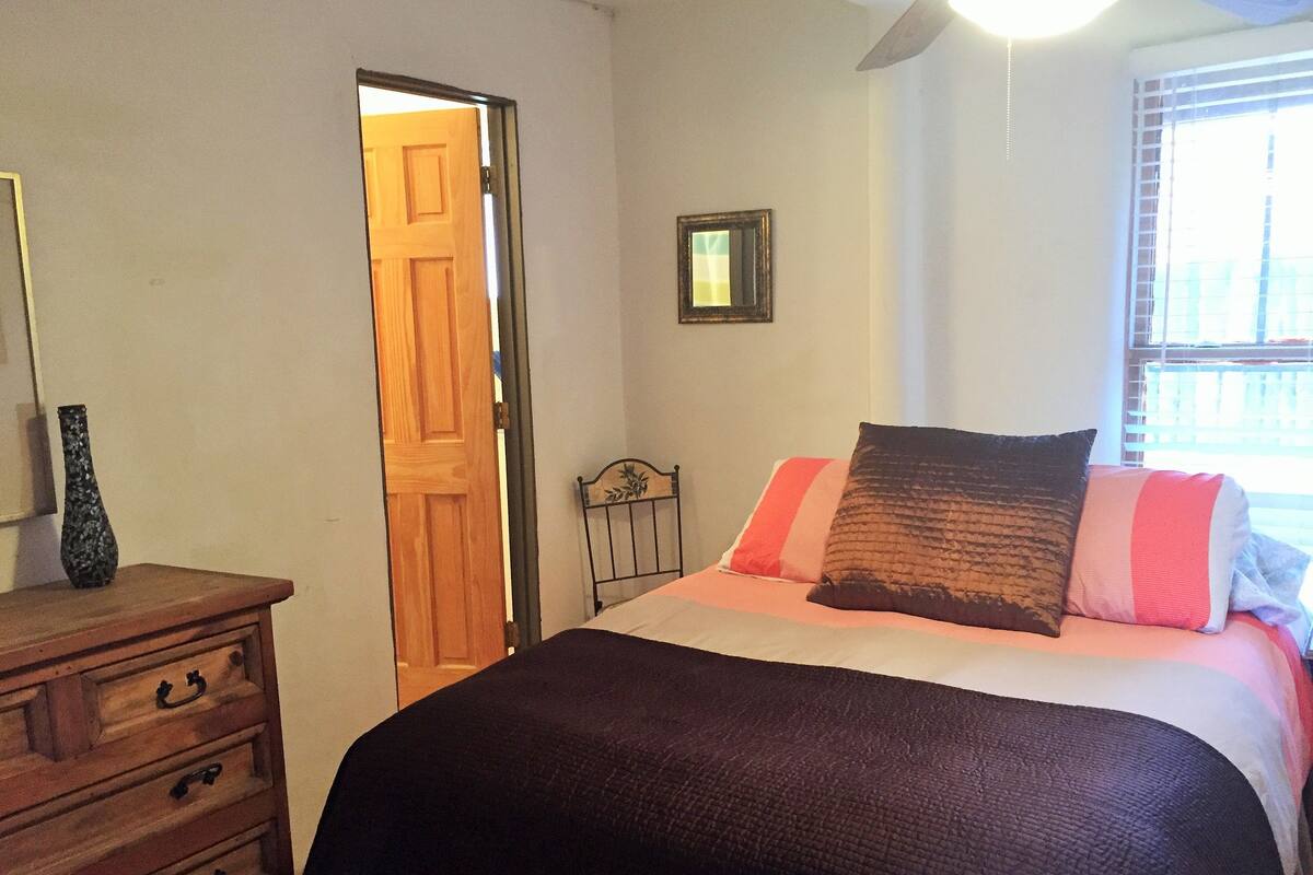 A bedroom with a bed, dresser, and a door leading to another room.