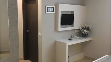 Un dormitorio moderno con una cama, un televisor montado en una consola blanca, una puerta y una pequeña planta en maceta.