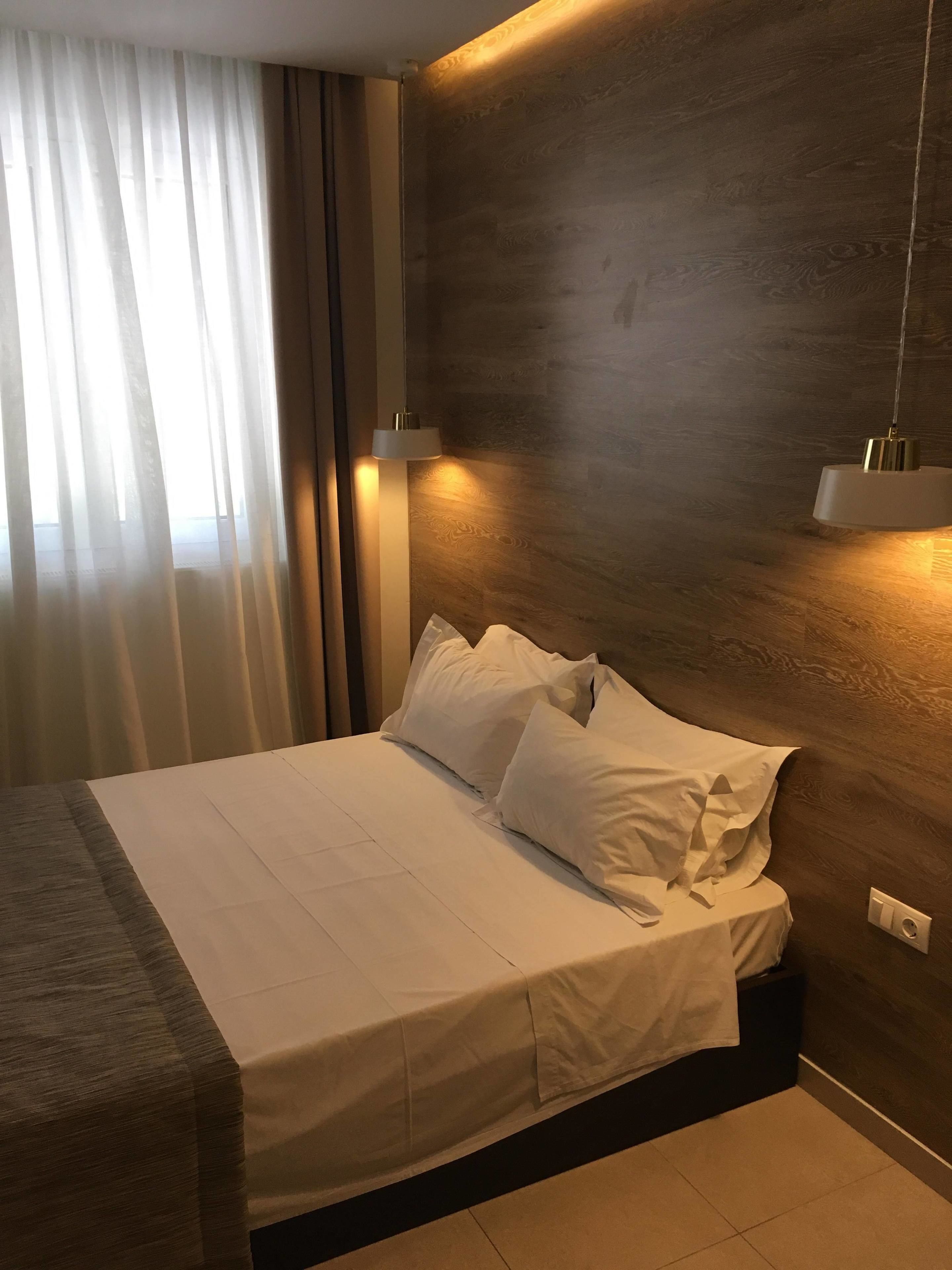 A neatly made bed with white linens, a wooden headboard, and two bedside lamps.