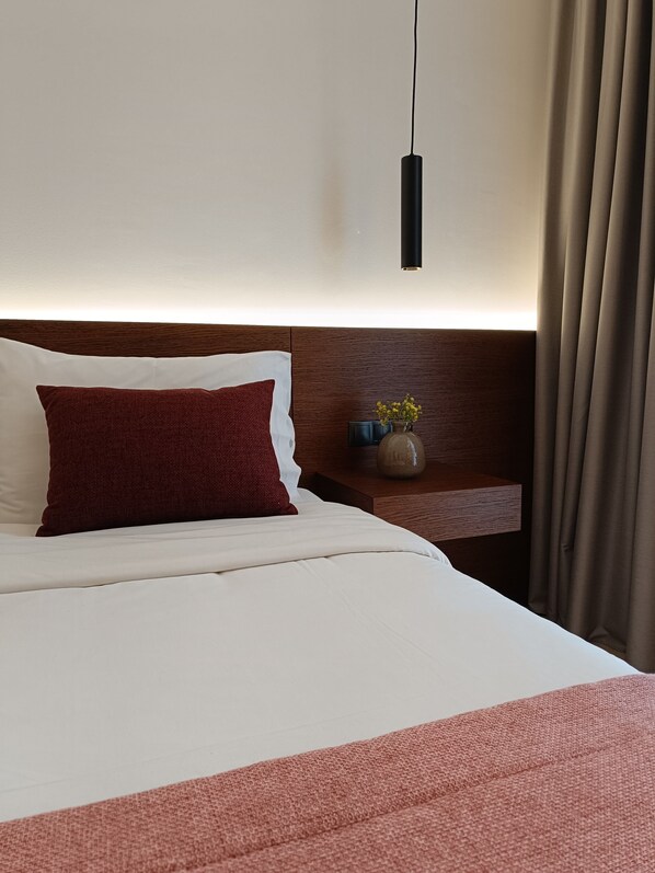 A neatly made bed with white and red pillows, a bedside table with a vase of flowers, and a hanging light fixture.