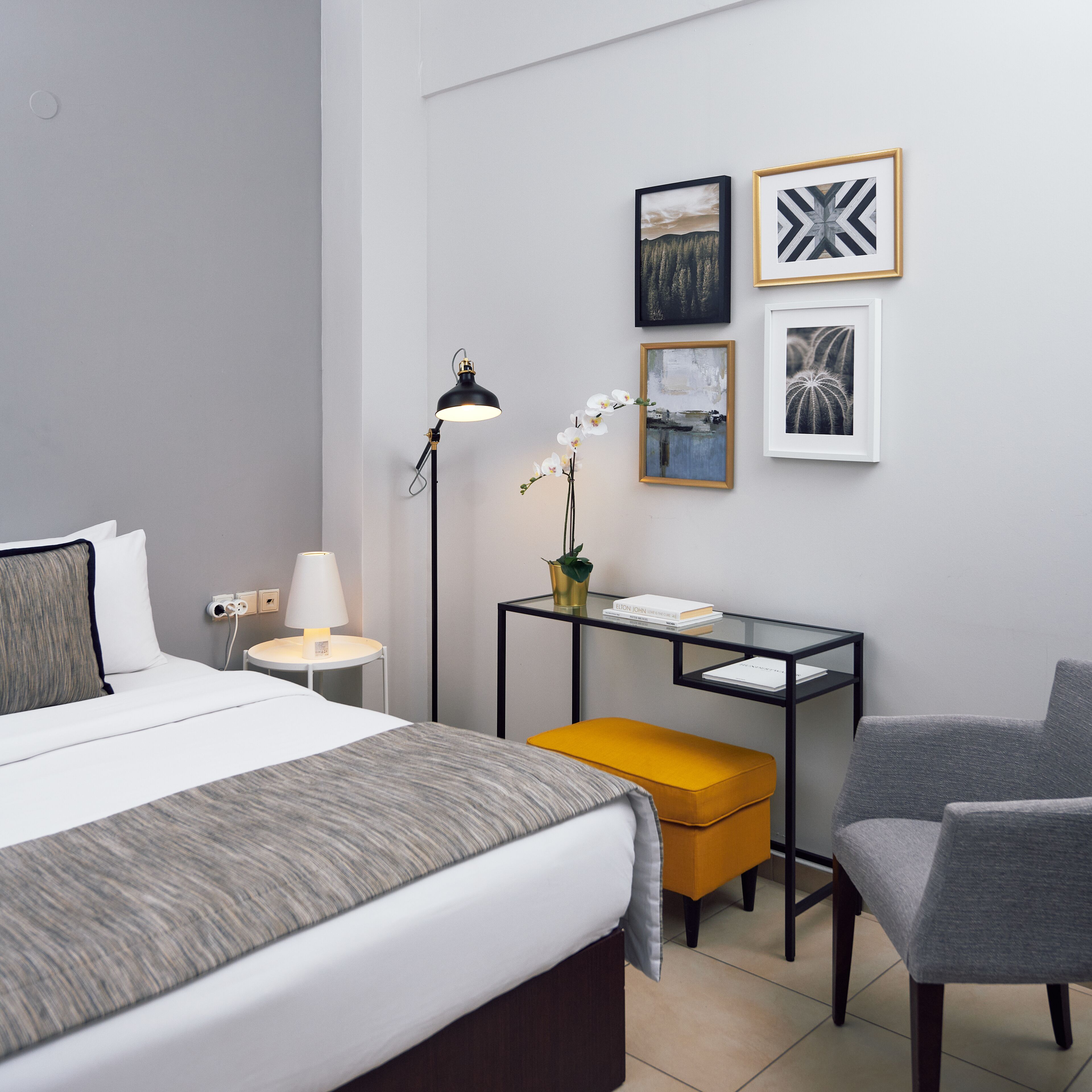 A hotel room with a bed, a desk, a chair, and artwork on the wall.
