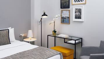 A hotel room with a bed, a desk, a chair, and artwork on the wall.