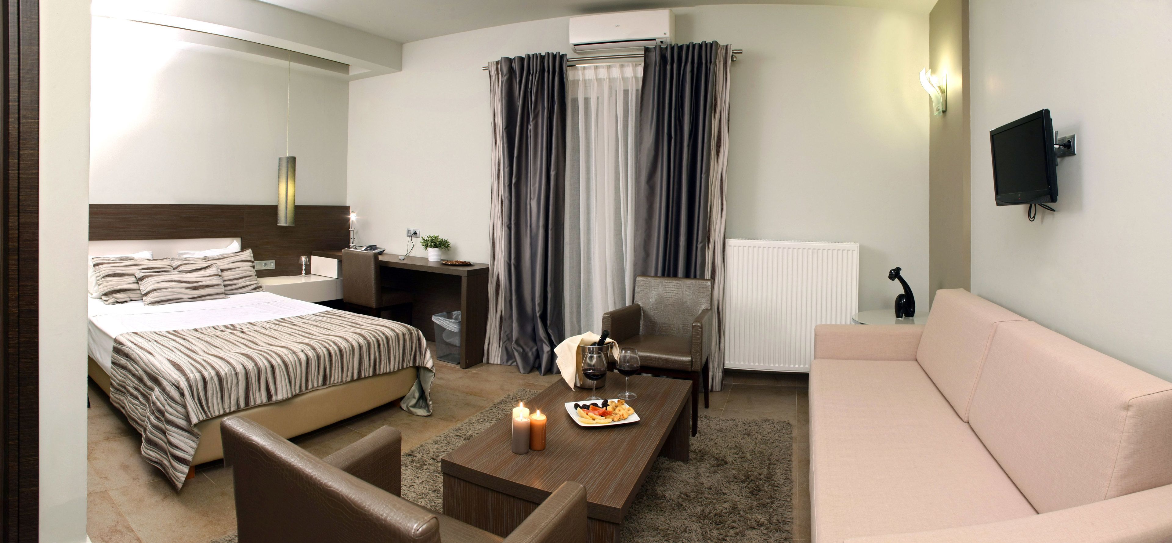 A hotel room with a bed, a desk, a chair, a sofa, a TV, and a window with curtains.