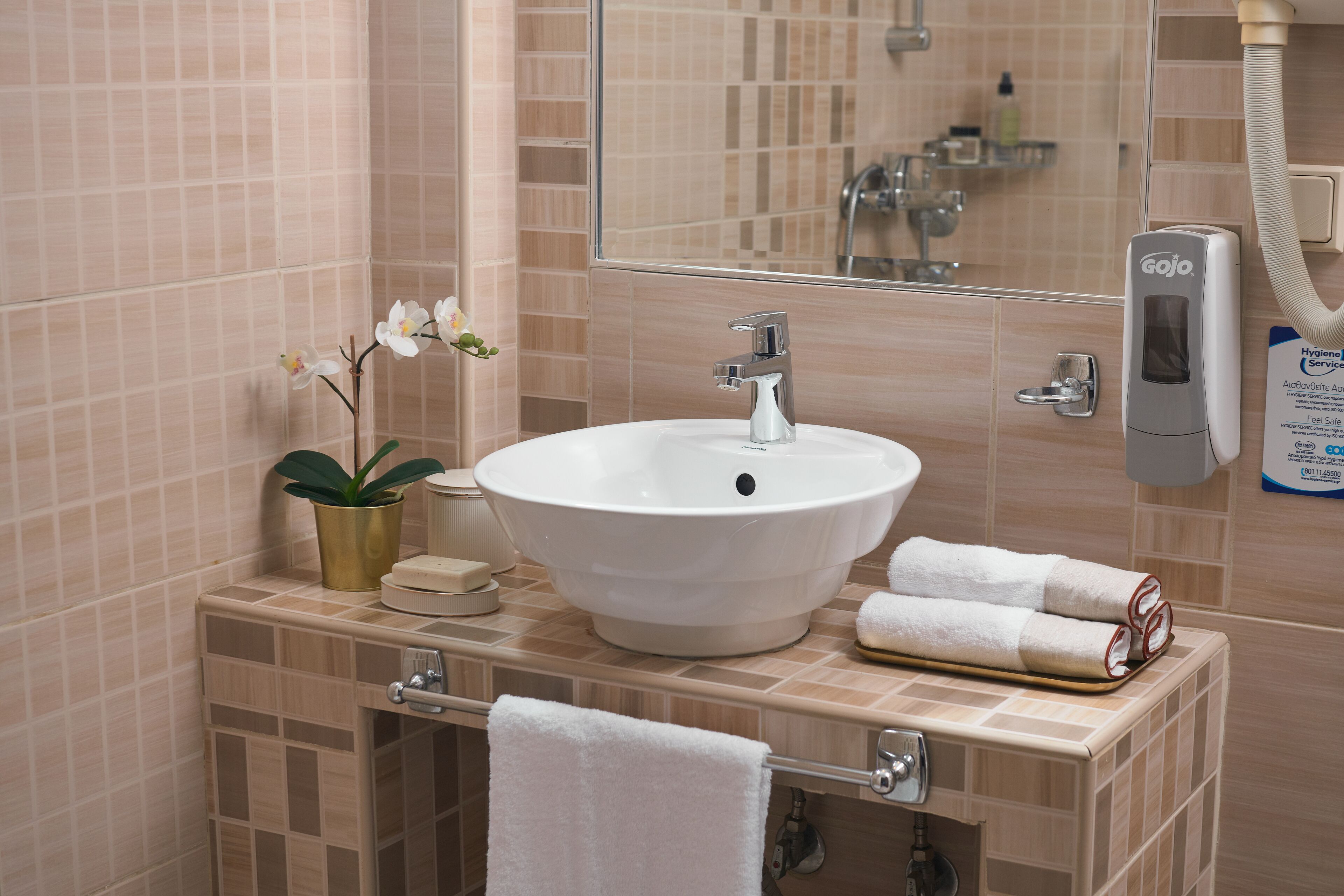 Une salle de bain avec un lavabo blanc, un miroir, un sèche-mains Gojo et un porte-serviettes.