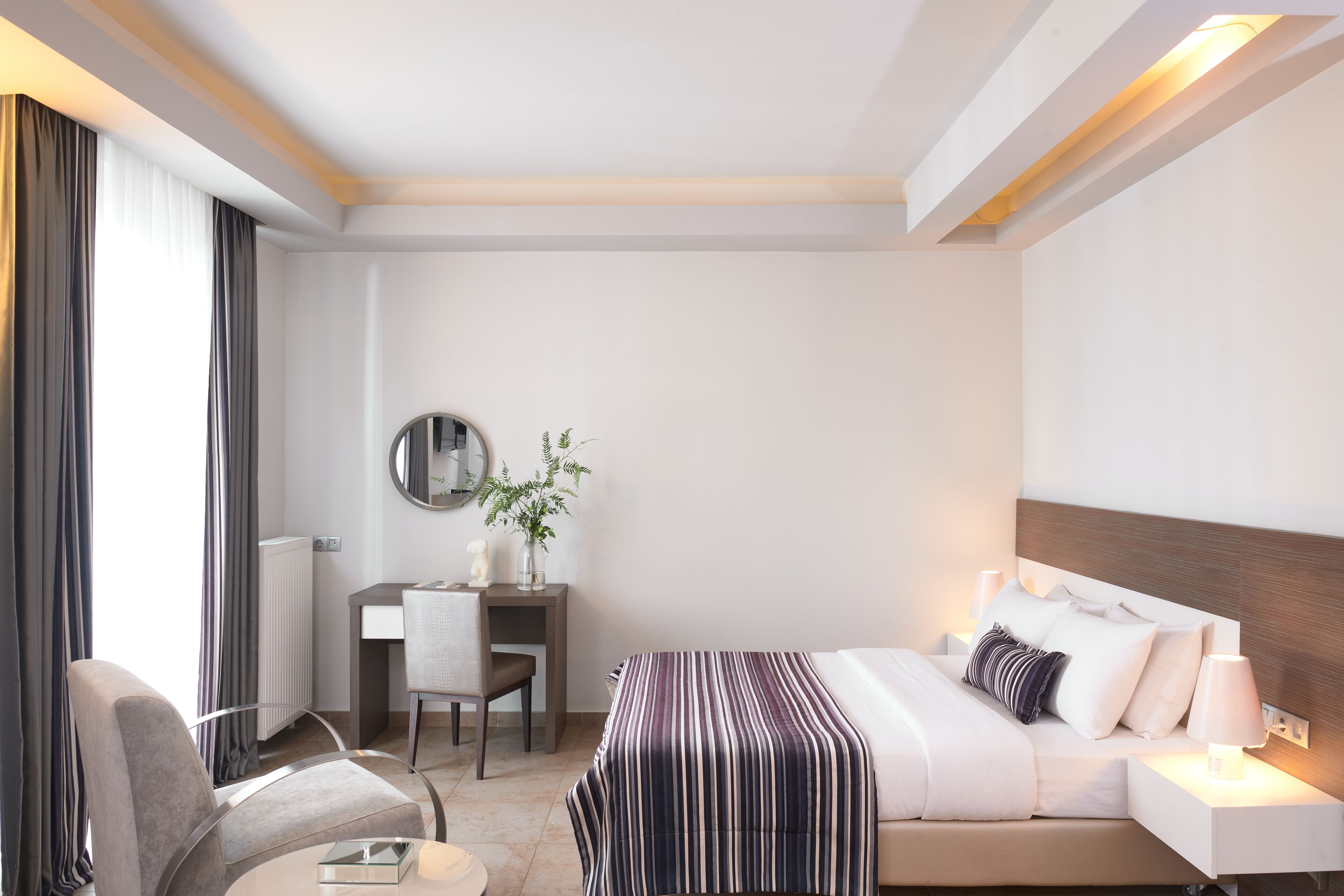 A hotel room with a bed, bedside table, chair, desk, and a mirror.