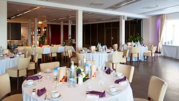 A spacious banquet hall with round tables set for dining, featuring white tablecloths and beige chairs.