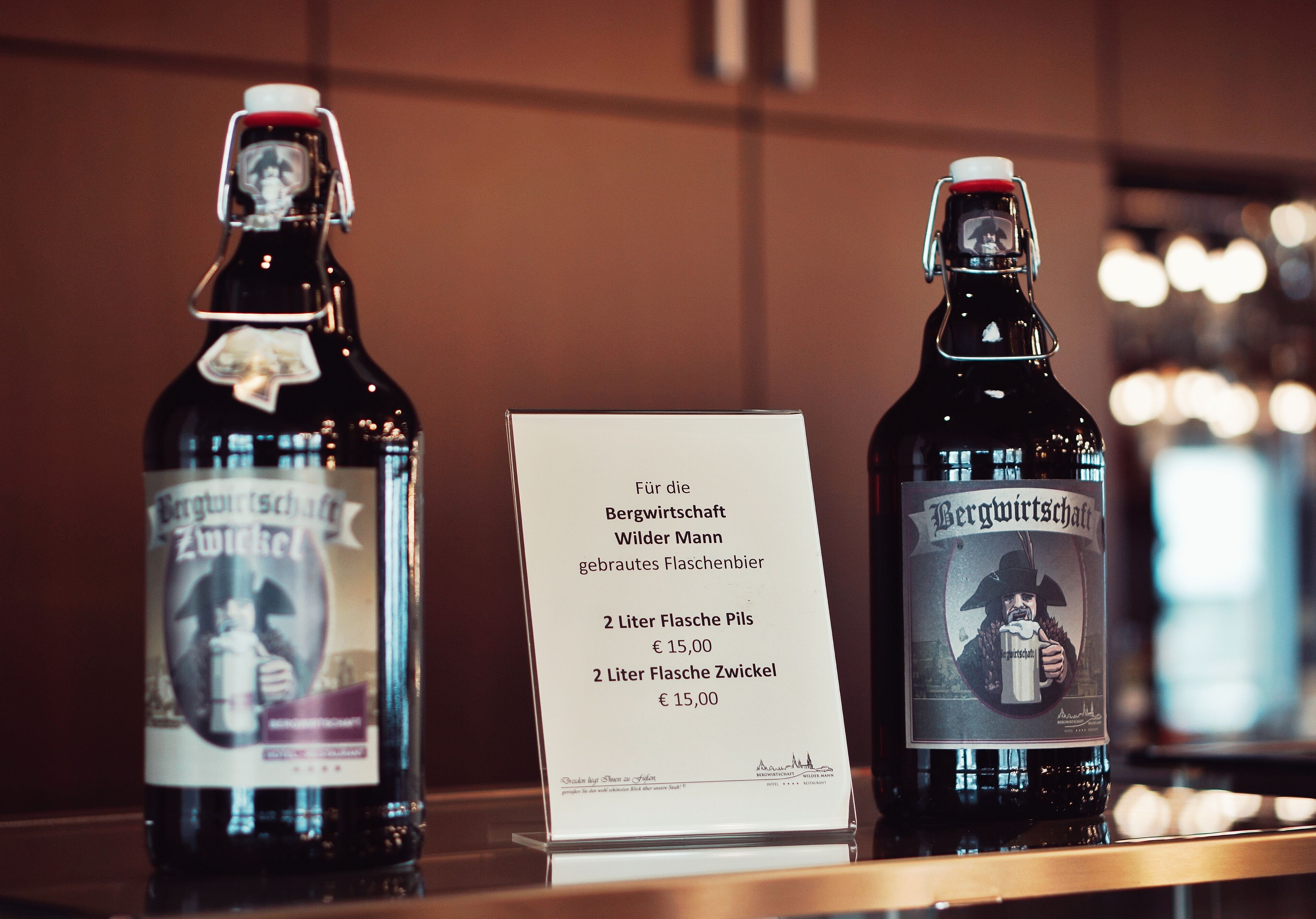 Deux bouteilles de bière Bergwurst, accompagnées d’une étiquette indiquant qu’elles sont destinées au restaurant Bergwirtschaft Wilder Mann, vendues au prix de 15,00 € les 2 litres.