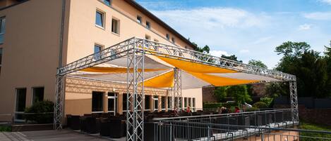 A building with a covered outdoor seating area, a balcony, and a stone wall.