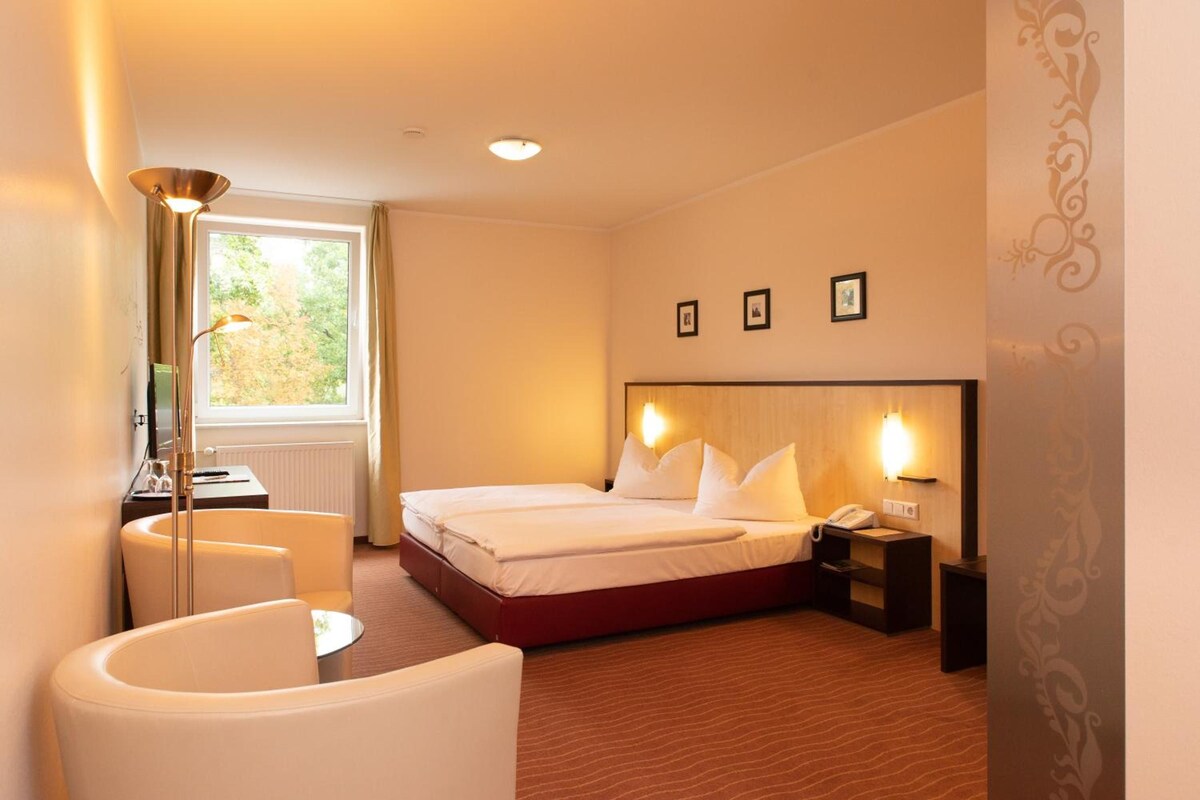Una camera d'albergo con un letto, comodini, una scrivania, una sedia, una lampada e una finestra con tende.