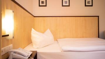 A hotel room with a wooden headboard, a bedside telephone, and three framed pictures on the wall.