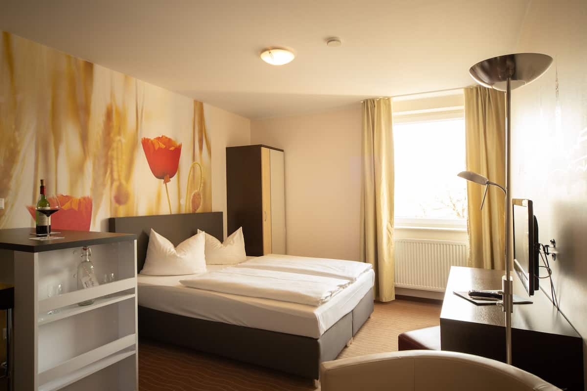 Ein Hotelzimmer mit Bett, Schreibtisch, Stuhl, Fernseher, Kleiderschrank und einem Fenster mit Vorhängen.
