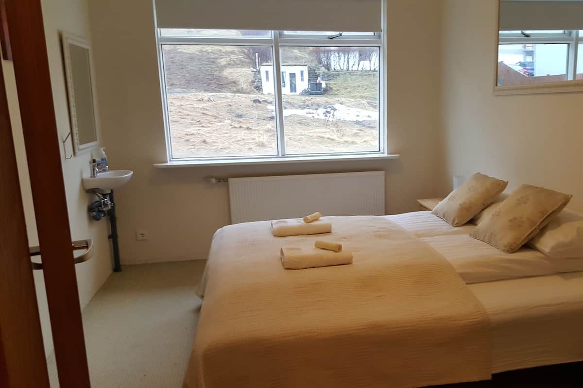 Een slaapkamer met een bed, twee kussens, een raam, een radiator en een wastafel.