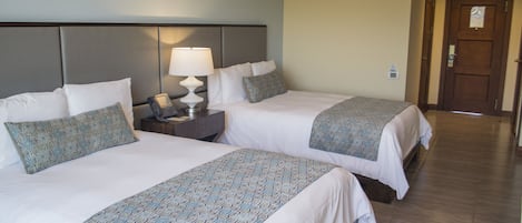 A hotel room with two beds, a nightstand with a lamp, and a telephone.