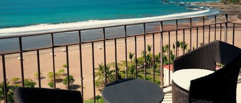 A balcony with wicker furniture overlooking a beach and ocean.