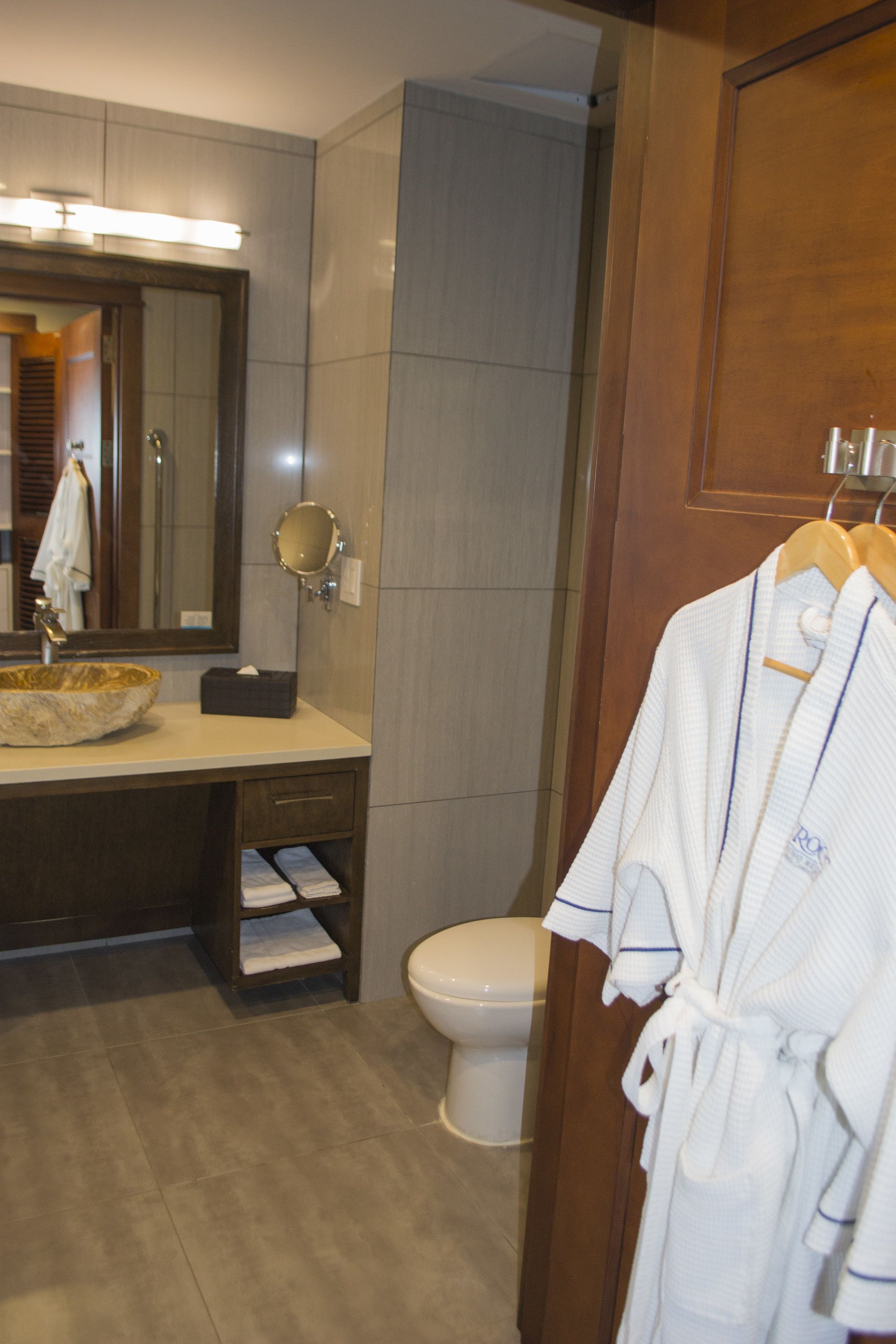 Une salle de bain avec un meuble-lavabo en bois, un miroir rond, un lavabo blanc et des toilettes blanches.