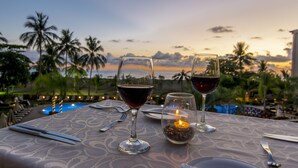 A table set for two with wine glasses and a candle, overlooking a pool and palm trees at sunset. - Crocs Resort & Casino (Jacó)
