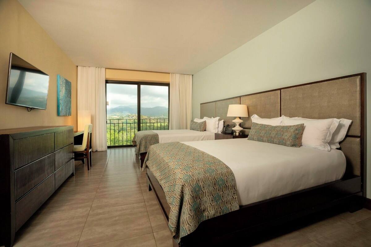 Ein Hotelzimmer mit zwei Betten, einem Fernseher, einem Schreibtisch und einem Balkon mit Blick.