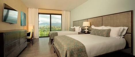 Habitación de hotel con dos camas, televisión, escritorio y balcón con vistas.
